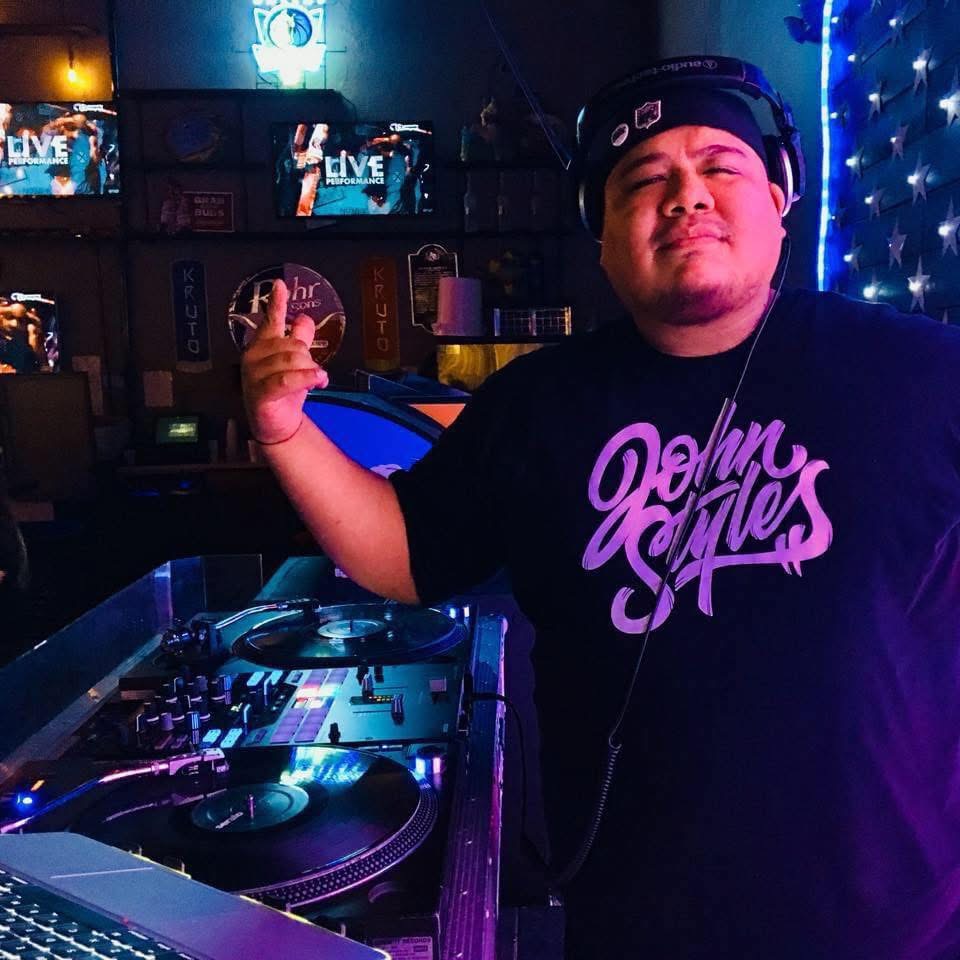 DJ John Styles wearing branded shirt and headphones behind the decks